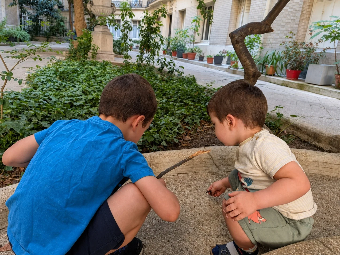 Two children playing together in a leafy courtyard