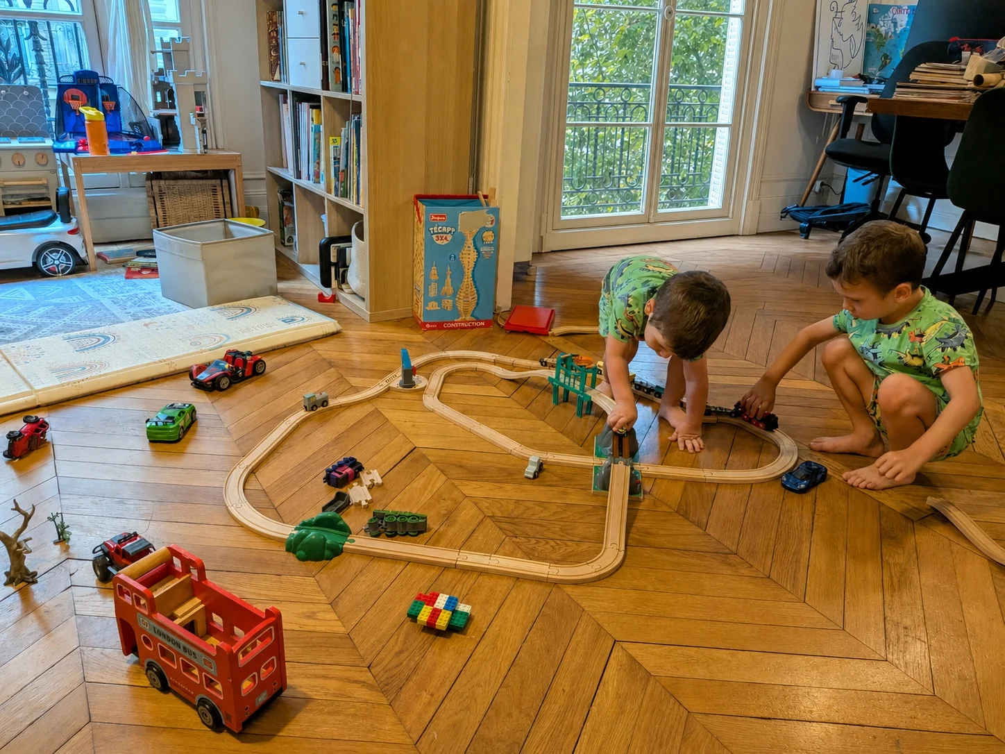 Two children playing together with a wooden train set at home